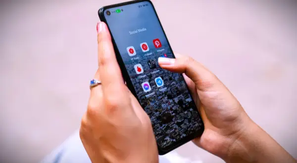 Dłoń z pierścionkiem na ekranie telefonu z ikonami aplikacji, w tym Messenger. Czy jak usunę wiadomość na Messengerze to on to widzi?