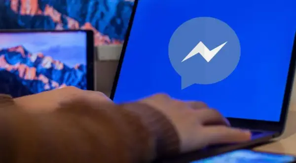 Dłoń na laptopie z logo Messengera. Dowiedz się, jak odzyskać cofniętą wiadomość Messenger.