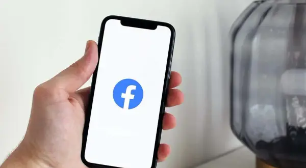 Dłoń trzyma smartfon z logo Facebooka. Dowiedz się, jak dodać zdjęcie profilowe na FB z galerii.