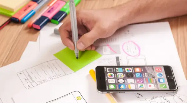 Ręka pisze na zielonej karteczce, obok leży smartfon i szkice. To inspiracja, jak wymyślić ksywkę.
