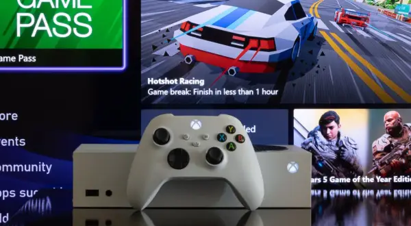 Biały kontroler Xbox i konsola na tle ekranu z menu Game Pass i grami. Dowiedz się, jak pobierać gry na Xbox, korzystając ze sklepu i Game Pass.