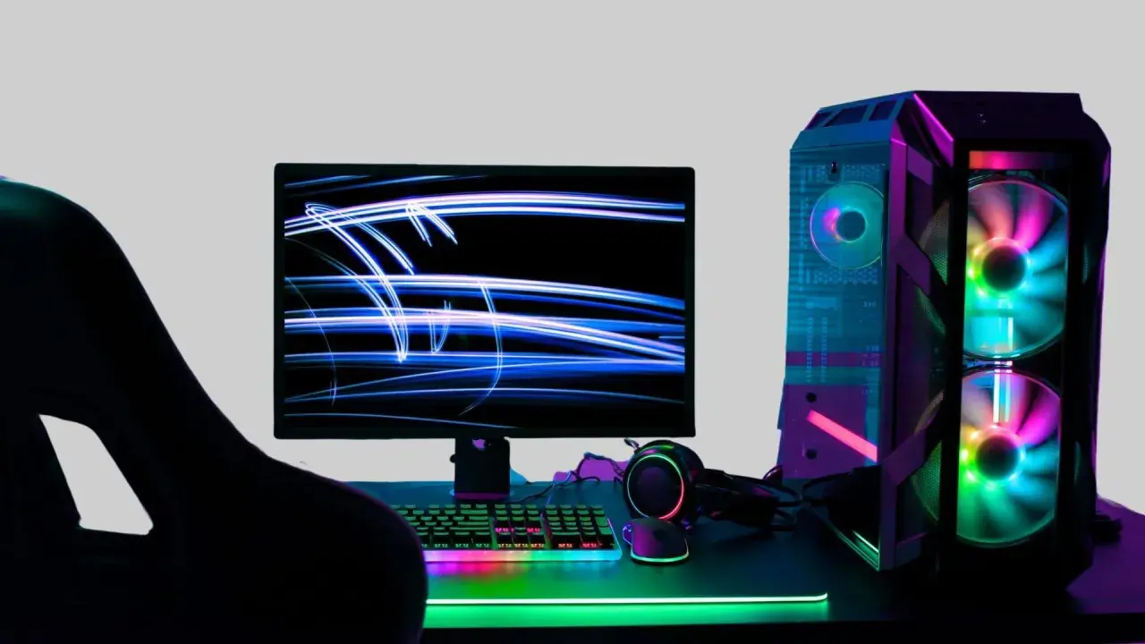 Gracz wpatrzony w monitor z niebieskimi smugami światła. Obok komputer z kolorowymi wentylatorami. Idealne miejsce na fajne słowa po angielsku na nick.