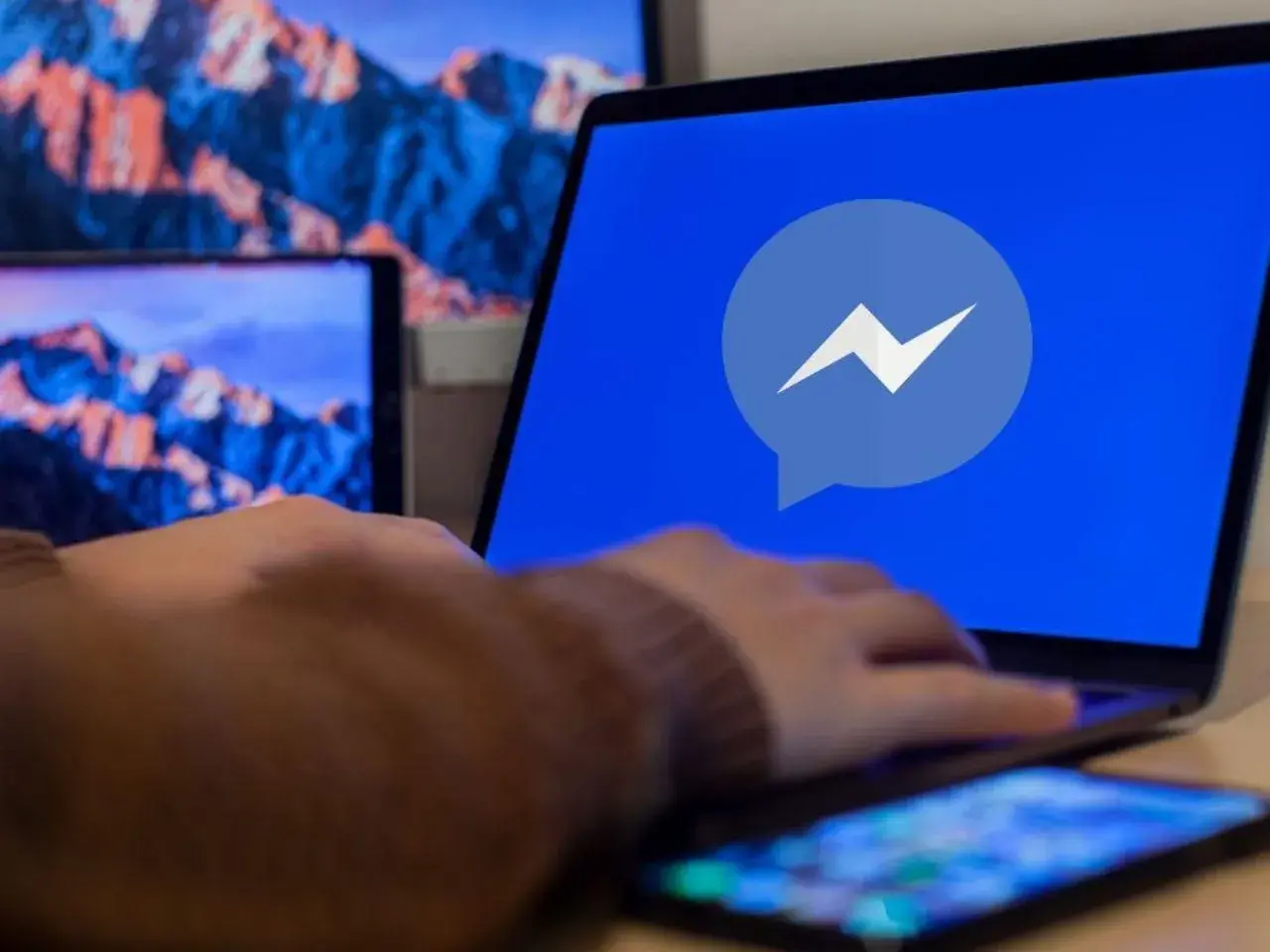 Dłoń na laptopie z logo Messengera. Dowiedz się, jak odzyskać cofniętą wiadomość Messenger.