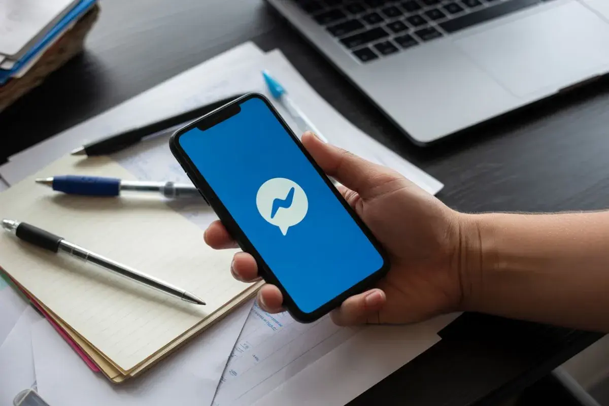 Dłoń trzyma smartfon z ikoną Messengera. Dowiedz się, jak znaleźć czat grupy na Messengerze, korzystając z telefonu.