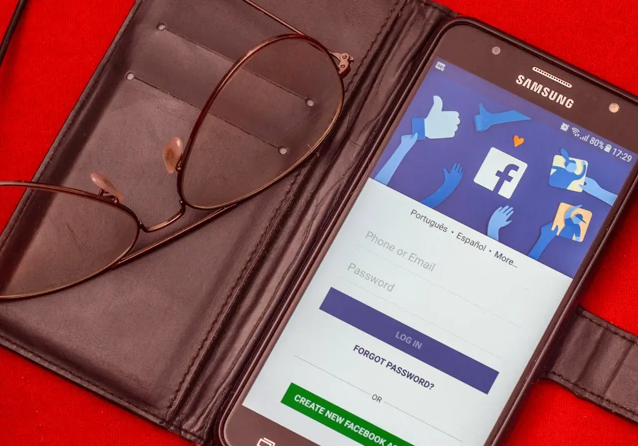 Okulary leżą na portfelu obok telefonu z ekranem logowania do Facebooka. Zastanawiasz się, czy usunięcie konta na FB i Messengera to dobry pomysł?