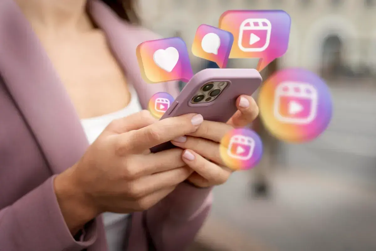 Dłonie trzymające telefon, nad którym unoszą się ikony Instagrama. Szukasz sposobu, jak odzyskać konto na Instagramie?