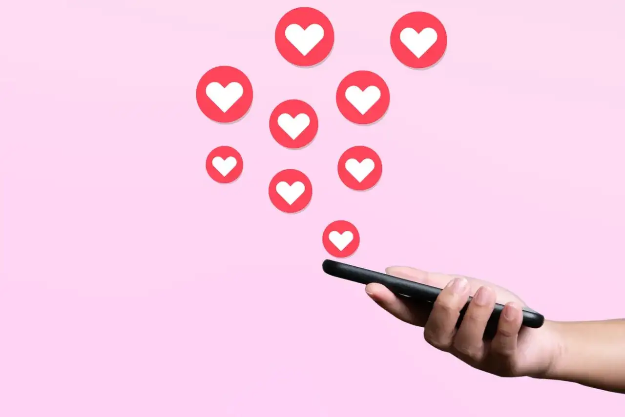 Darmowe lajki na Instagramie? Smartfon w dłoni, a z niego wypływają serduszka, symbolizujące popularność i uznanie.