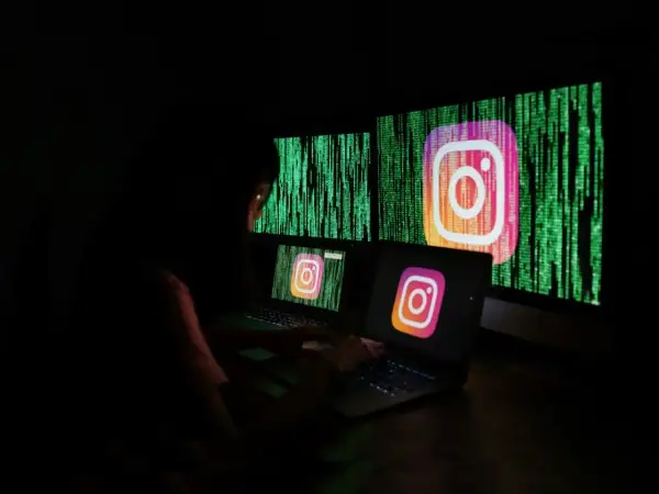 Osoba przy komputerze próbuje dowiedzieć się, jak odblokować konto na Instagramie. Na ekranach widnieje logo Instagrama na tle kodu.