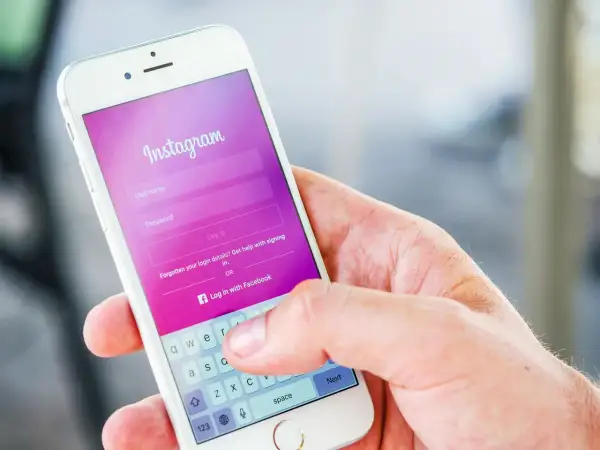 Dłoń trzyma smartfon z ekranem logowania Instagram. Widoczna opcja "Zapomniane dane logowania?" podpowiada, jak odzyskać hasło na Instagramie.