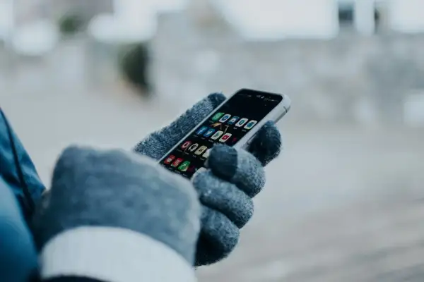 Ręka w rękawiczce trzyma smartfon z ikonami aplikacji. Chcesz wiedzieć, jak sprawdzić czy ktoś jest aktywny na Facebooku?