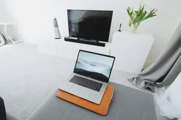 Nowoczesny salon z MacBookiem na pufie i telewizorem w tle. Dowiedz się, jak połączyć MacBooka z telewizorem, by cieszyć się filmami na dużym ekranie.