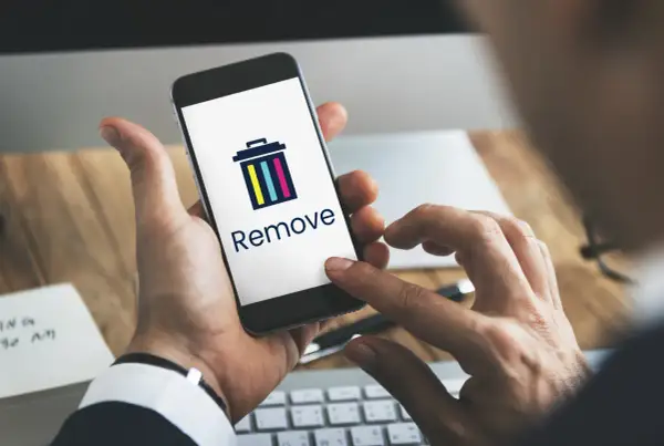 Dłoń trzyma smartfon z ikoną kosza i napisem "Remove". Dowiedz się, jak usunąć członka z grupy na Messengerze.
