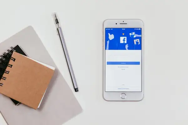 Smartfon z ekranem logowania Messengera. Jak odzyskać hasło do Messengera bez Facebooka? Notatnik i długopis obok.