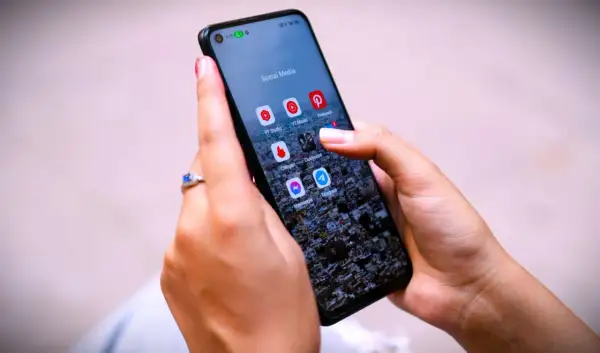 Dłoń z pierścionkiem na ekranie telefonu z ikonami aplikacji, w tym Messenger. Czy jak usunę wiadomość na Messengerze to on to widzi?