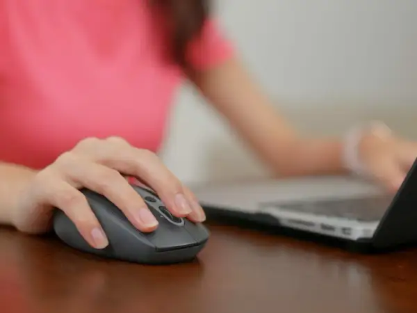 Dłoń na myszce, która jest podłączona do laptopa. Wiesz już, gdzie podłączyć myszkę do komputera.
