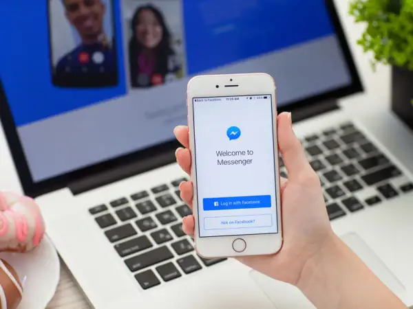 Dłoń trzyma iPhone'a z ekranem powitalnym Messengera. Dowiedz się, jak ustawić dymki czatu Messenger na iPhone.