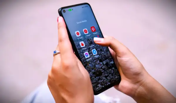 Dłonie trzymają telefon z ikonami aplikacji społecznościowych. Zastanawiasz się, jak trwale usunąć wiadomości z Messengera?
