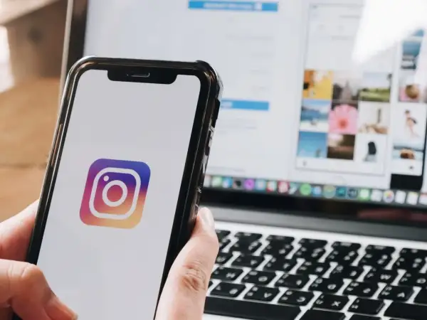 Telefon z logo Instagram. Na ekranie laptopa widać siatkę zdjęć, jakbyś chciał dowiedzieć się, jak wstawić czyjąś relację na swoją.