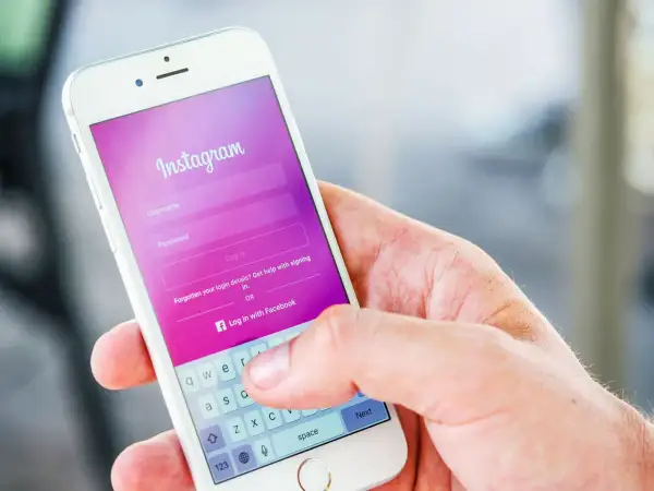 Dłoń trzyma smartfon z ekranem logowania Instagram. Dowiedz się, jak dodać zdj na Insta, logując się lub tworząc konto.