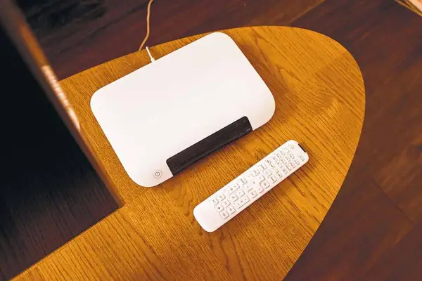 Biały router i pilot na drewnianym stoliku. Dowiedz się, jak zmienić hasło w routerze T-Mobile.