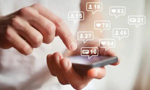 Dłoń z telefonem, na którym pojawiają się powiadomienia o polubieniach i komentarzach. Szybki sposób na kupno followersów na Instagramie.