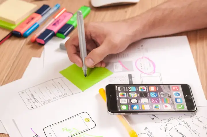 Ręka pisze na zielonej karteczce, obok leży smartfon i szkice. To inspiracja, jak wymyślić ksywkę.
